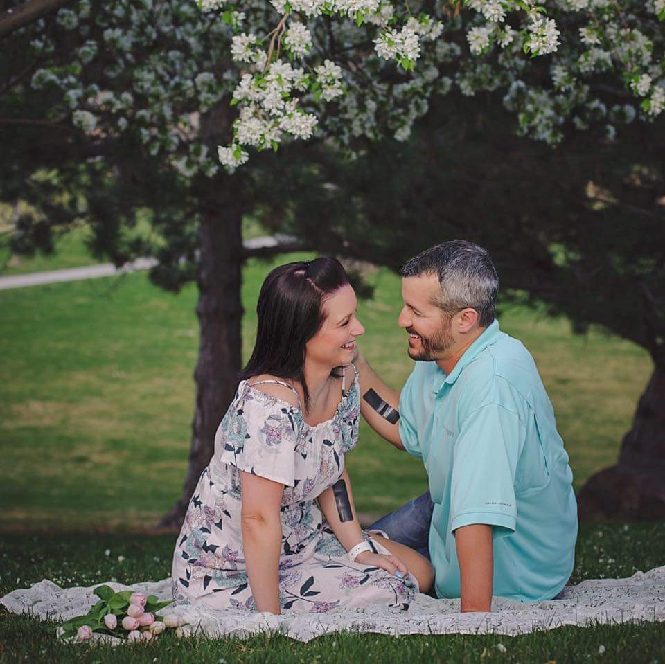 Shanann and Chris Watts sitting in a park smiling at each other.